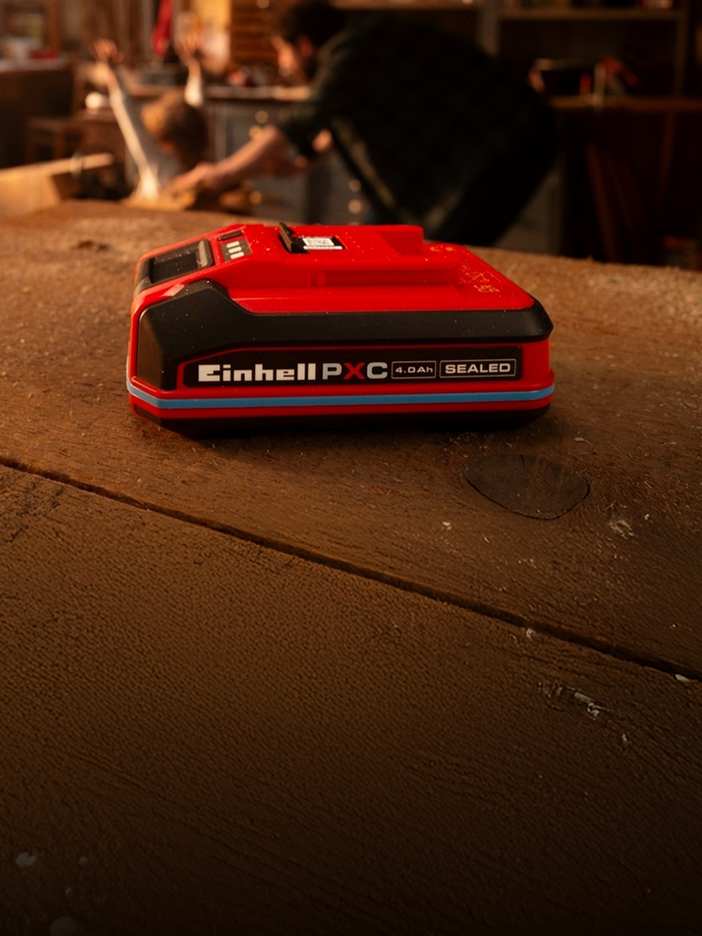 Batería Einhell Power X-Change de 4.0 Ah SEALEAD sobre un banco de trabajo de madera, con anillo y etiqueta azules.