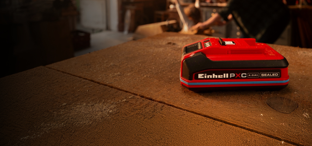 Batería Einhell Power X-Change de 4.0 Ah SEALEAD sobre un banco de trabajo de madera, con anillo y etiqueta azules.