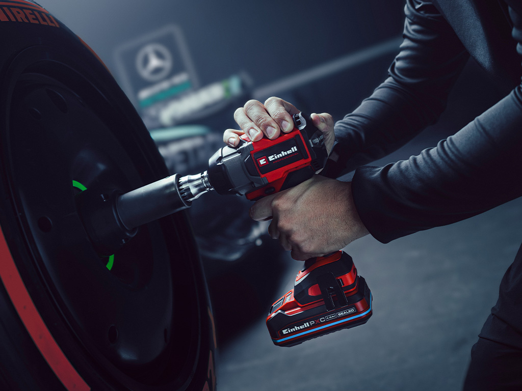 Llave de impacto inalámbrica Einhell en uso sobre una rueda de auto, con el branding y el logotipo de colaboración del equipo Mercedes-AMG Petronas de Fórmula 1