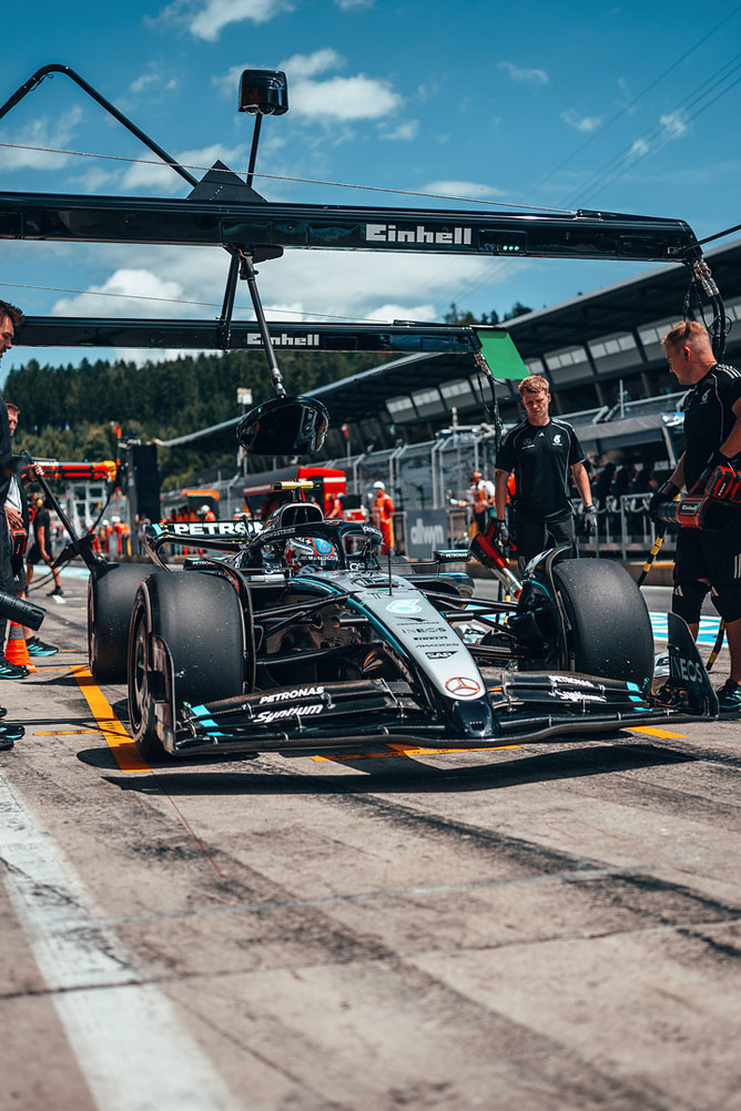 Un coche Mercedes-AMG de Fórmula 1 está en el pit lane, rodeado de miembros del equipo bajo una estructura de garaje Einhell.