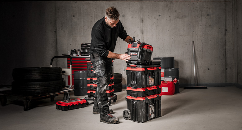 A man places a smaller Einhell case onto a tall, wheeled E-Case system with multiple modules.