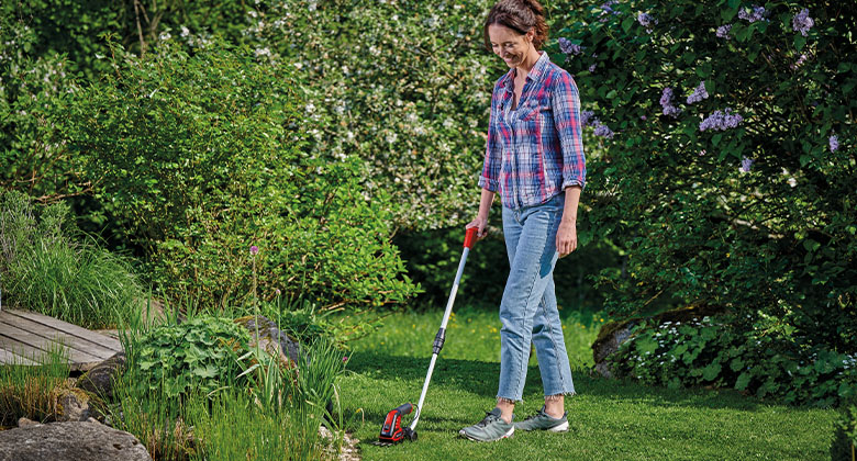a woman is trimming lawn edges with a Einhell cordless grass- and bush shear